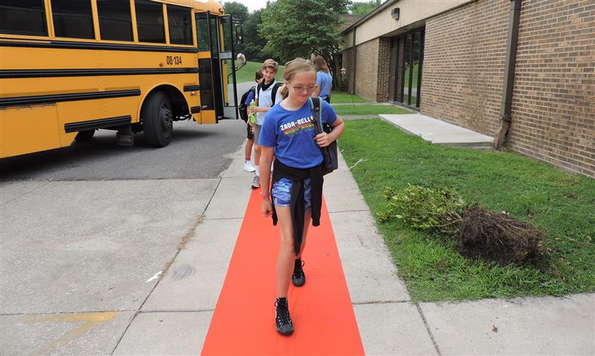 Students walking down the red carpet off of a school bus